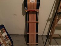 Full view of the three-seater wood toboggan standing upright with its black metal runners and wood planks visible.