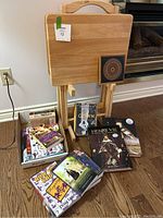 The two wooden tray tables on a rack with the small thread square art piece placed on one table and a box with books and magazines underneath.