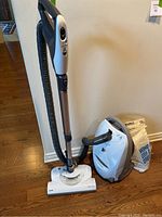 Full view of canister vacuum with hose, wand, floor head and bag packaging