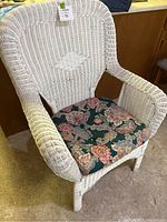Front view of white wicker chair with floral cushion on seat, showing overall condition and structure.
