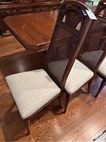 Six wood dining chairs shown, highlighting the beige patterned fabric seats and cane backs with carved wood detail.