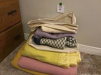 Stack of three wool blankets in yellow and pink colors with three folded wool sweaters on top.