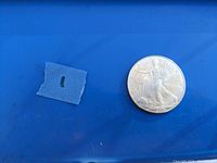 Photo of 2003 American Silver Eagle coin on blue background with small piece of blue tape.