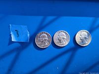 Three silver quarters from 1941, 1943, and 1951 arranged on blue surface with blue tape marked '3'.