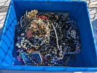 Blue plastic bin filled with a huge lot of assorted costume jewelry including necklaces, bracelets, beaded and faux pearl pieces.