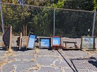 Nine large and medium decorative shelves arranged on outdoor ground next to chain-link fence, showing variety of wood frames and mirrored backs.