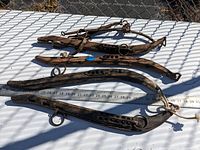 Four primitive antique horse hames laid out on white surface with measuring tape beneath for scale, showing length and condition