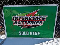 Close-up of rectangular green tin Interstate Batteries sign showing dents and rust spots.