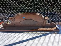 Photo of a wooden wall shelf with intricate carved top and scroll details on sides, placed on the ground outdoors
