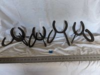 Four handmade horseshoe coat hooks arranged in a row with a ruler for scale, showing their length approximately 12 inches.