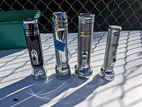 Four vintage flashlights arranged upright on pavement, showing chrome finishes and one black and chrome model.