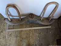 Primitive double ox yoke showing full front view with central metal ring and two wooden bows, laying on floor with measuring sticks measuring approximately 46 inches length.
