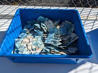 Full blue bin filled with many individually packaged vintage watch crystals in sealed wrappers and paper.