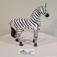 Front side view of the large hand carved and painted zebra figurine showcasing detailed black stripes on white wood, standing on four legs with tail slightly curved.