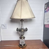 Full view of vintage glass and brass lamp with beige replaced fabric shade, showing decorative ram heads and brass accents on a textured glass base around 32 inches tall.