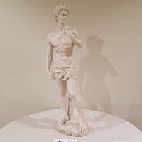 Full view of the 20 inch tall polystone statue of Michaelangelo's David, showing its off-white color, detailed musculature, curly hair, and cloth draped around the waist. The statue stands on a rough base.