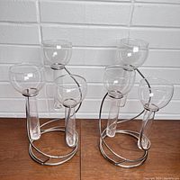 Front view of two tiered metal candle holders, each holding three clear glass vase holders on a white brick background.