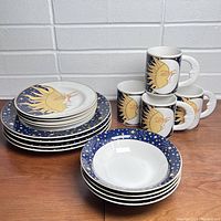 Photo showing all pieces: stack of dinner plates, salads bowls, side plates, and a set of 4 mugs with celestial sun and moon designs.