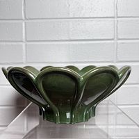 Front view of green ceramic fruit bowl with petal-shaped scalloped rim and glossy green glaze.
