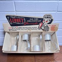 Top view of the open original box showing 4 Libbey soda fountain glasses with silver textured metal handles and holders inside.