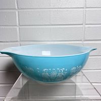 Side view of turquoise blue Pyrex Butterprint mixing bowl with white detailed farmers, roosters, and baskets pattern.