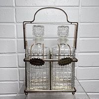 Front view of two cut glass decanters in metal Tantalus holder with Bourbon and Scotch labels.