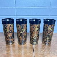 Front view of four vintage West Bend Thermo-Serv drinking glasses with black and gold ornate pattern and black rims