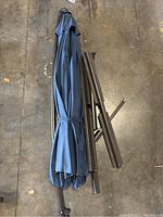 Folded navy blue umbrella canopy with disassembled brown metal frame pieces on concrete floor