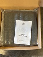 Two black Sodoct pyramid acoustic foam panels in plastic packaging inside an open box, with mounting instruction sheet visible.