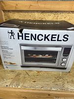 Original packaging front view showing HENCKELS convection countertop oven image, brand name and logo, and product features.