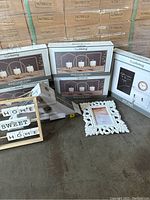 Photo showing boxes of trueliving metal candle holders, wooden 'Home Sweet Home' block sign, white photo frame and wall shelf box.