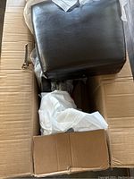 Unassembled black leather chair packed in original box with protective plastic wrapping.