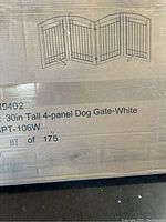 Photo of the original packaging showing an illustration of the assembled dog gate, labeling it as a 30 inch tall 4-panel white dog gate with item number SS19-SPT-106W.