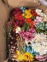 Box containing various colorful faux flower stems in red, orange, yellow, purple, pink, blue, cream, and white colors along with leafy stems.