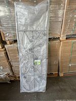 Single black metal garden trellis wrapped in bubble wrap with visible decorative scrollwork pattern.