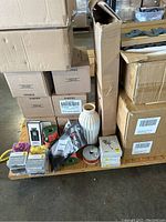 Boxes including Keurig coffee boxes piled on a wooden pallet, assorted small packaged items and a white vase in front.