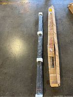 Projection screen rolled and wrapped in plastic with foam protectors on ends, laid on warehouse floor.
