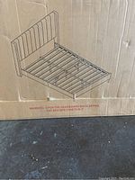 Packaging box with assembly diagram of bed frame showing slatted wooden base and upholstered headboard