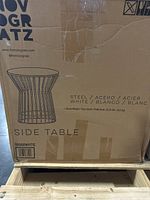 Cardboard packing box for a white steel side table by Novogratz, showing drawing of the table and brand name