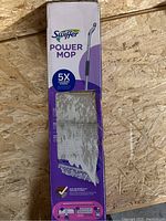 Front of boxed Swiffer Power Mop showing mop handle and device with promotional text indicating 5x cleaning power.