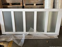 Full view of the horizontally positioned white framed barn style door showing five vertical frosted glass panes, wrapped partially in protective white foam.