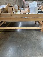 Photo showing the full length side of the wooden storage bin with four vertical 4x4 wooden posts and cross braces near the base. The concrete floor and warehouse environment seen in the background.