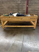 Front view of the wooden storage bin filled with miscellaneous items showing solid wood construction and casters.