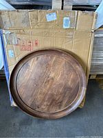 Round wooden coffee table top on a cardboard box, showing the wood grain and raised lip edge of the tabletop.