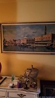 Full view of the framed Venetian canal scene painting over a piece of furniture with decorative objects below.