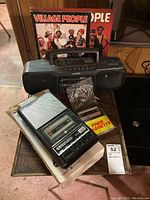 Sony boombox, GE tape recorder, Village People 45 and souvenir booklet arranged on a wooden table