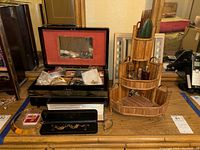 Full view of costume jewelry on wooden dresser showing black lacquered jewelry box with mirror and red interior, multiple small jewelry bags with pins and necklaces, a black case with gold-tone necklace, and bamboo tiered organizer with small bottles.