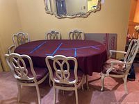Dining table covered with a red tablecloth surrounded by six chairs in a room with yellow walls and carpeted floor.
