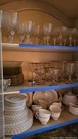 Photo of upper shelves showing multiple types of gold rimmed stemware glasses arranged in rows