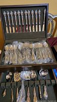 Wooden box open showing top row of 12 knives and middle row of sealed utensils